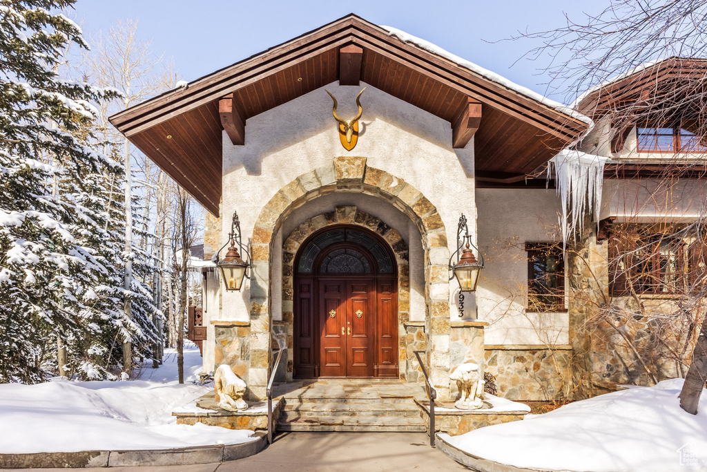 Snow covered property entrance featuring stucco siding and stone siding