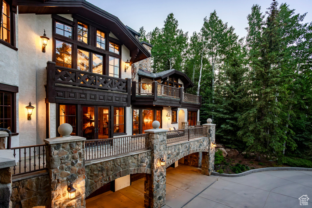 Back of property with a balcony, stucco siding, and stone siding