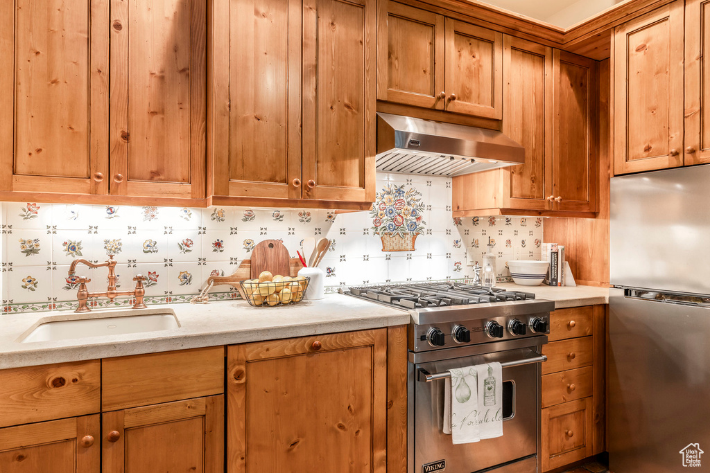 Kitchen with appliances with stainless steel finishes, under cabinet range hood, backsplash, and brown cabinetry