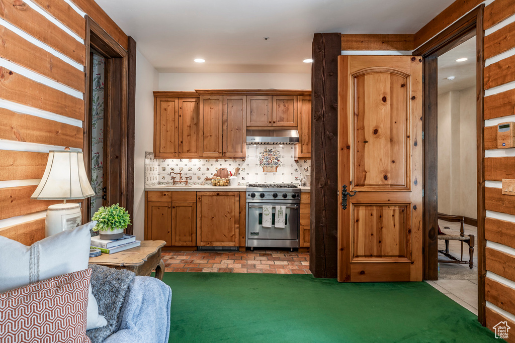 Kitchen with high end stove, range hood, tasteful backsplash, recessed lighting, and brown cabinets