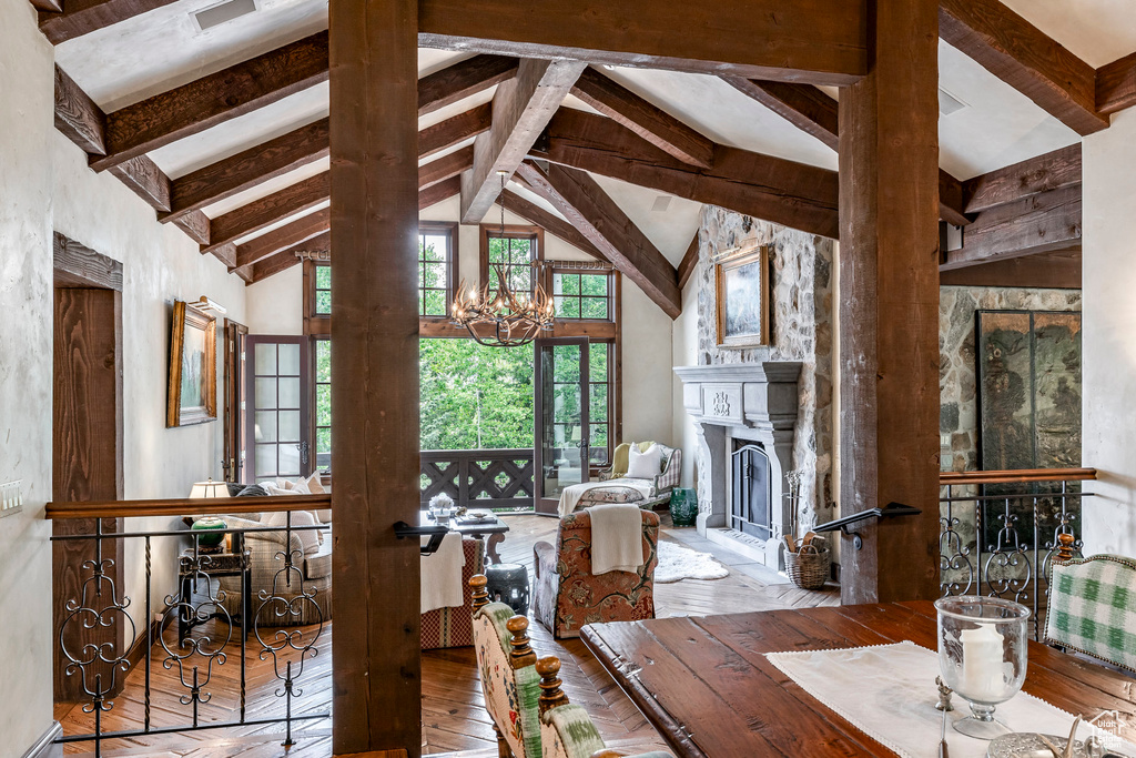 Dining room with beam ceiling, a fireplace, wood-type flooring, a chandelier, and high vaulted ceiling