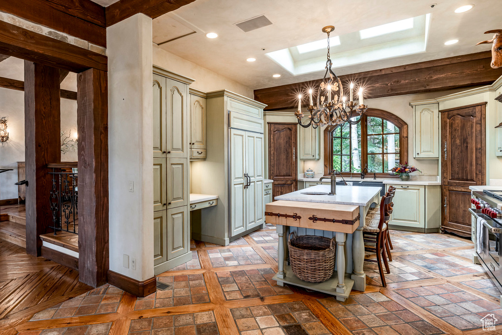 Kitchen with light countertops, a skylight, a tray ceiling, a chandelier, and an island with sink