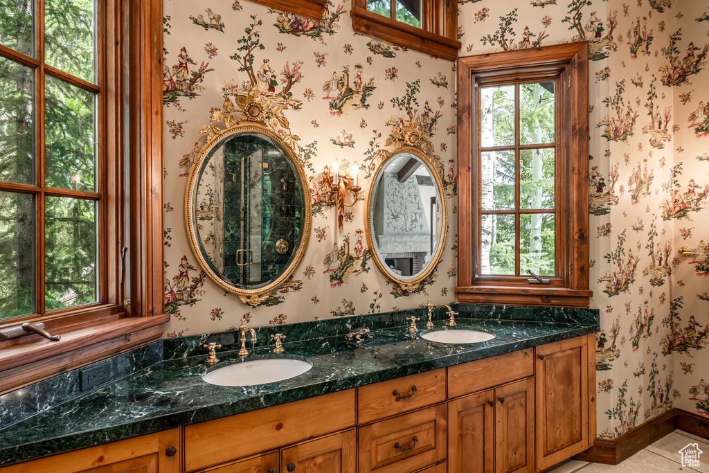 Bathroom with double vanity, wallpapered walls, and tile patterned flooring
