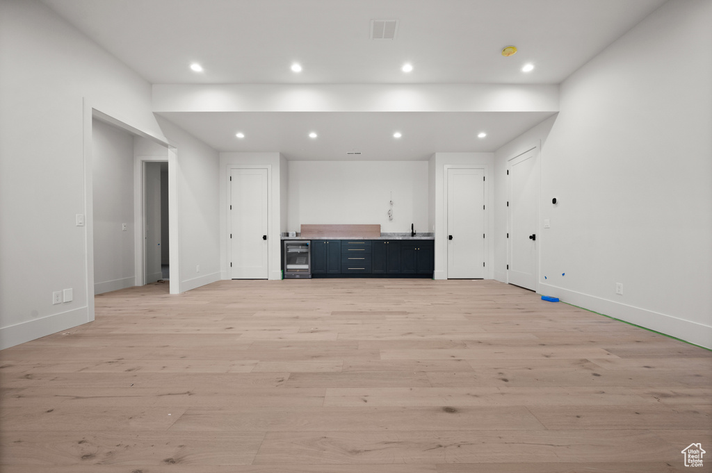 Unfurnished living room featuring beverage cooler, light wood-style floors, baseboards, and recessed lighting