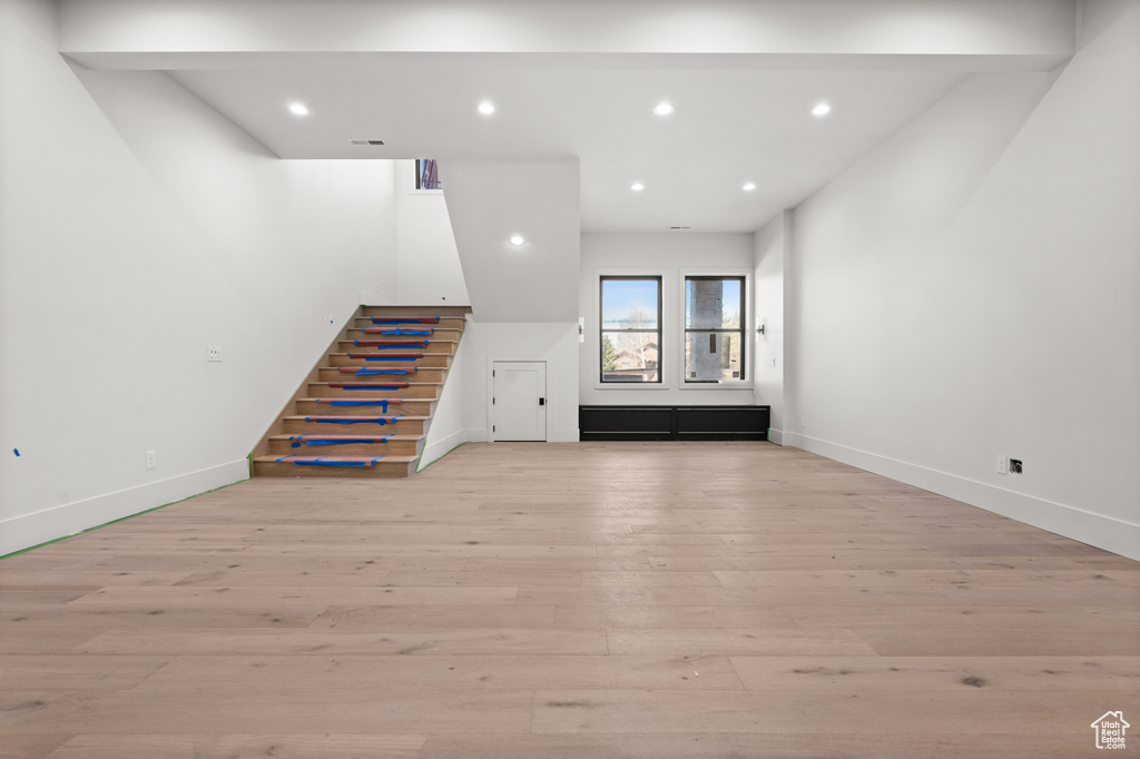 Unfurnished living room featuring stairs, light wood finished floors, baseboards, and recessed lighting