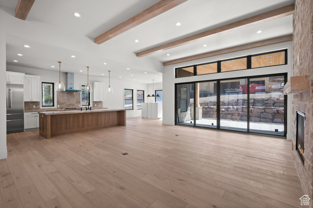 Unfurnished living room with beamed ceiling, light wood finished floors, recessed lighting, a fireplace, and a sink