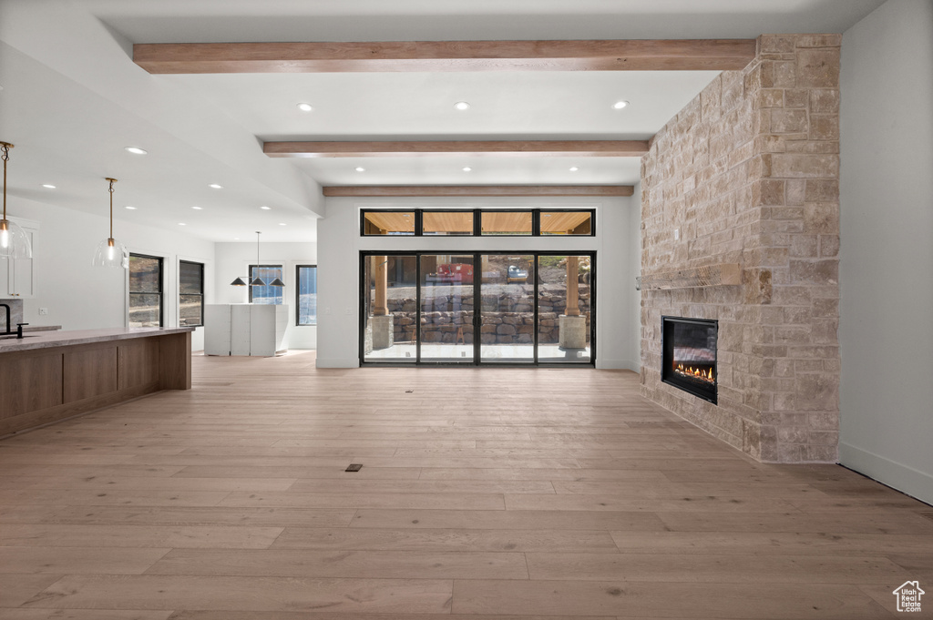 Unfurnished living room featuring a stone fireplace, beamed ceiling, light wood-type flooring, and recessed lighting