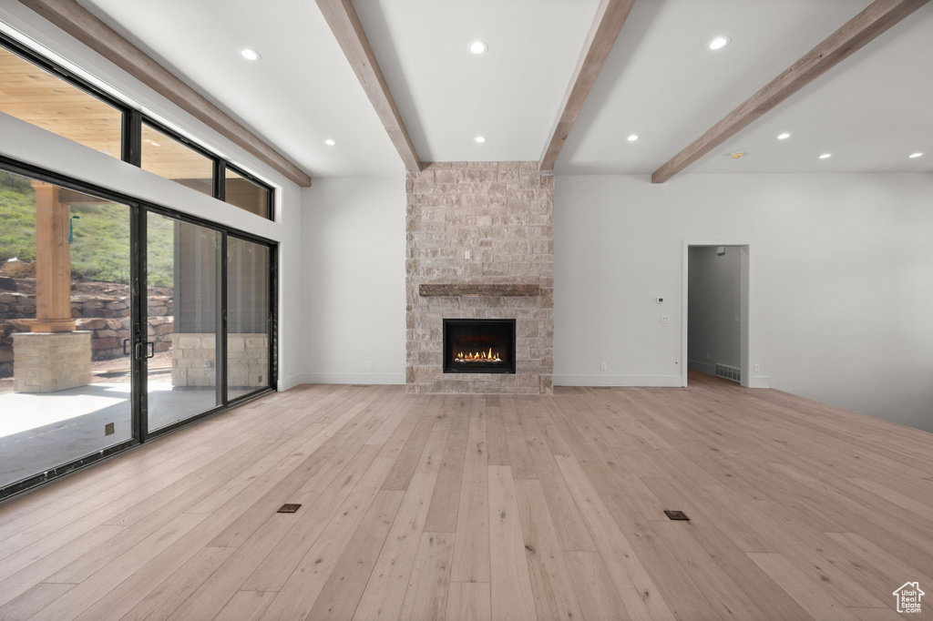 Unfurnished living room featuring a stone fireplace, hardwood / wood-style flooring, beamed ceiling, recessed lighting, and french doors