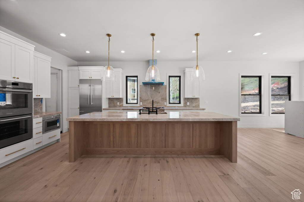 Kitchen featuring double oven, wall chimney exhaust hood, tasteful backsplash, light wood-style flooring, and stainless steel built in fridge
