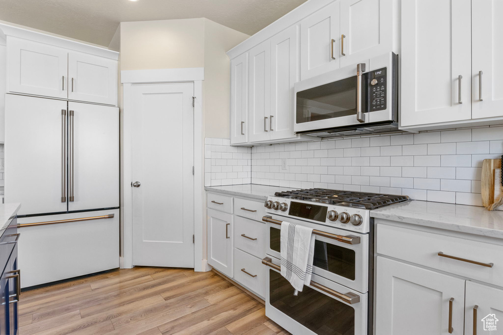 Kitchen with premium appliances, tasteful backsplash, light wood-style flooring, white cabinets, and light stone countertops