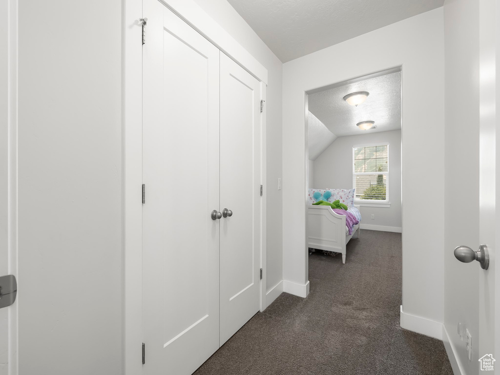 Corridor featuring dark colored carpet, lofted ceiling, and a textured ceiling