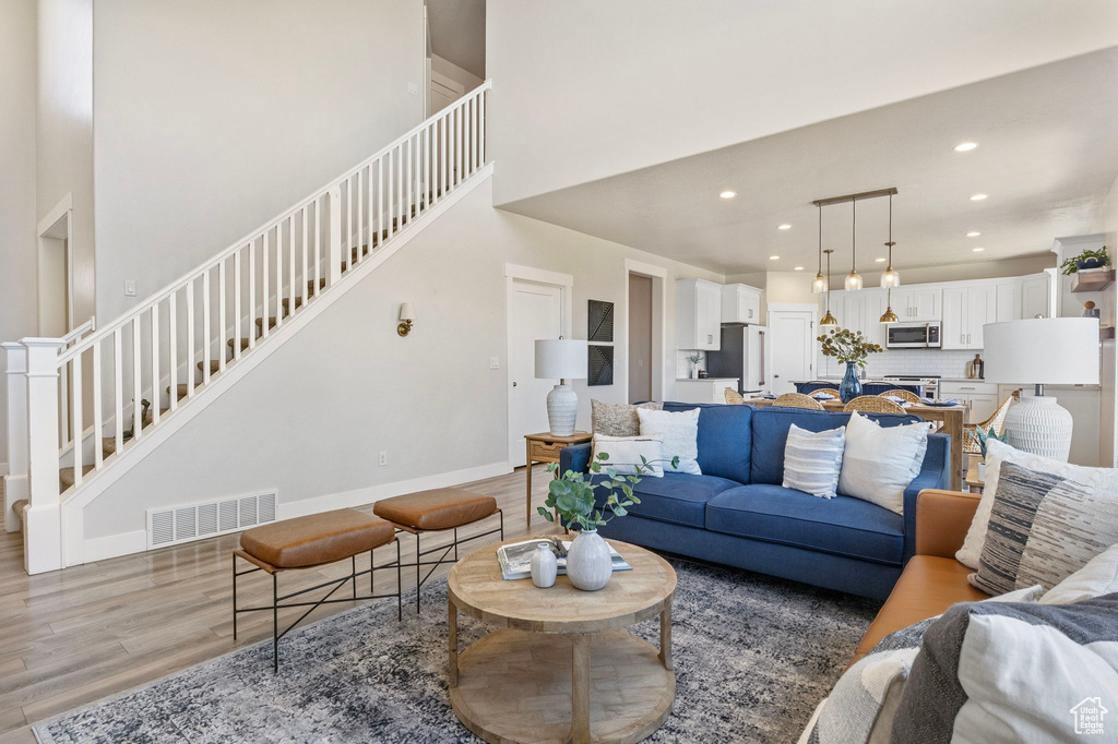 Living area with visible vents, a towering ceiling, light wood-style floors, baseboards, and stairs