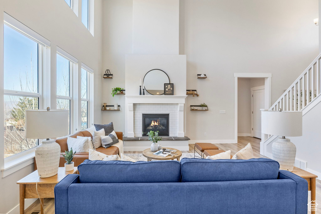 Living room featuring a high ceiling, a brick fireplace, wood finished floors, baseboards, and stairs