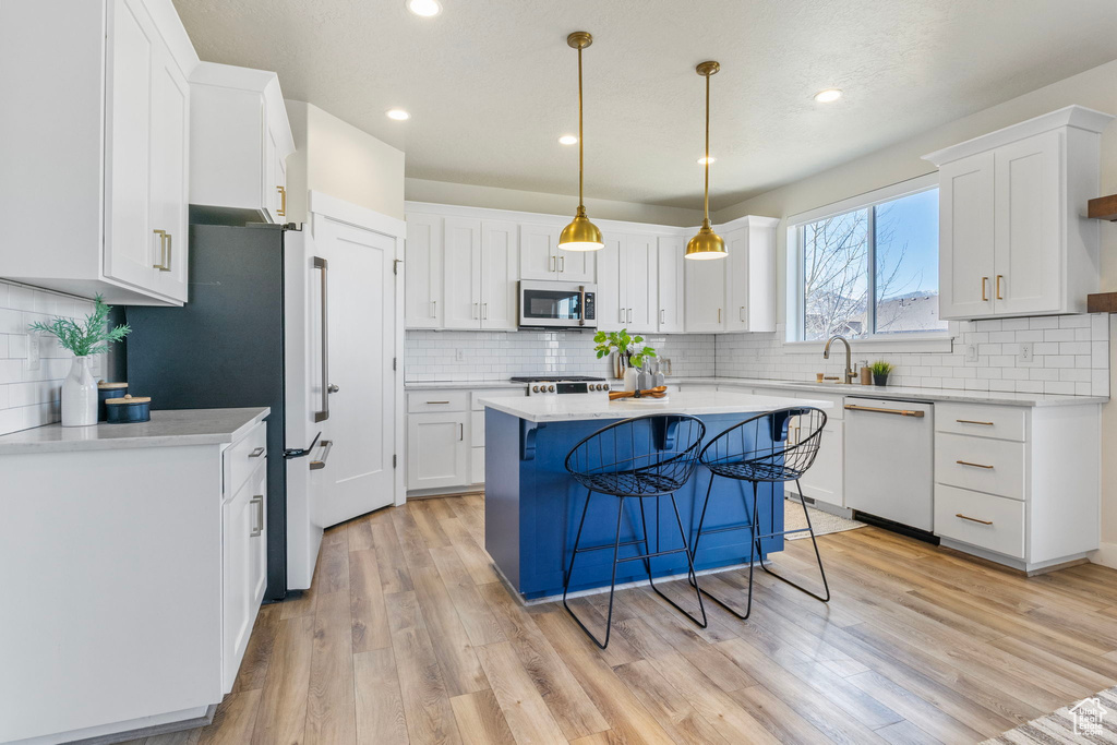 Kitchen featuring white dishwasher, a kitchen island, white cabinets, and light wood-style floors