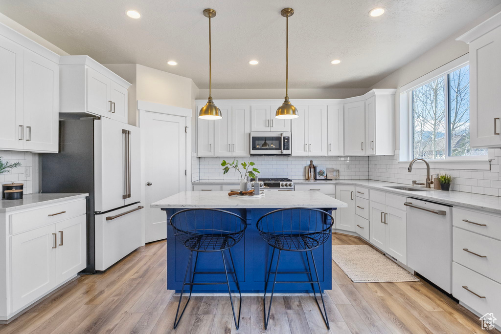 Kitchen with white appliances, a kitchen island, a sink, and light wood-style floors