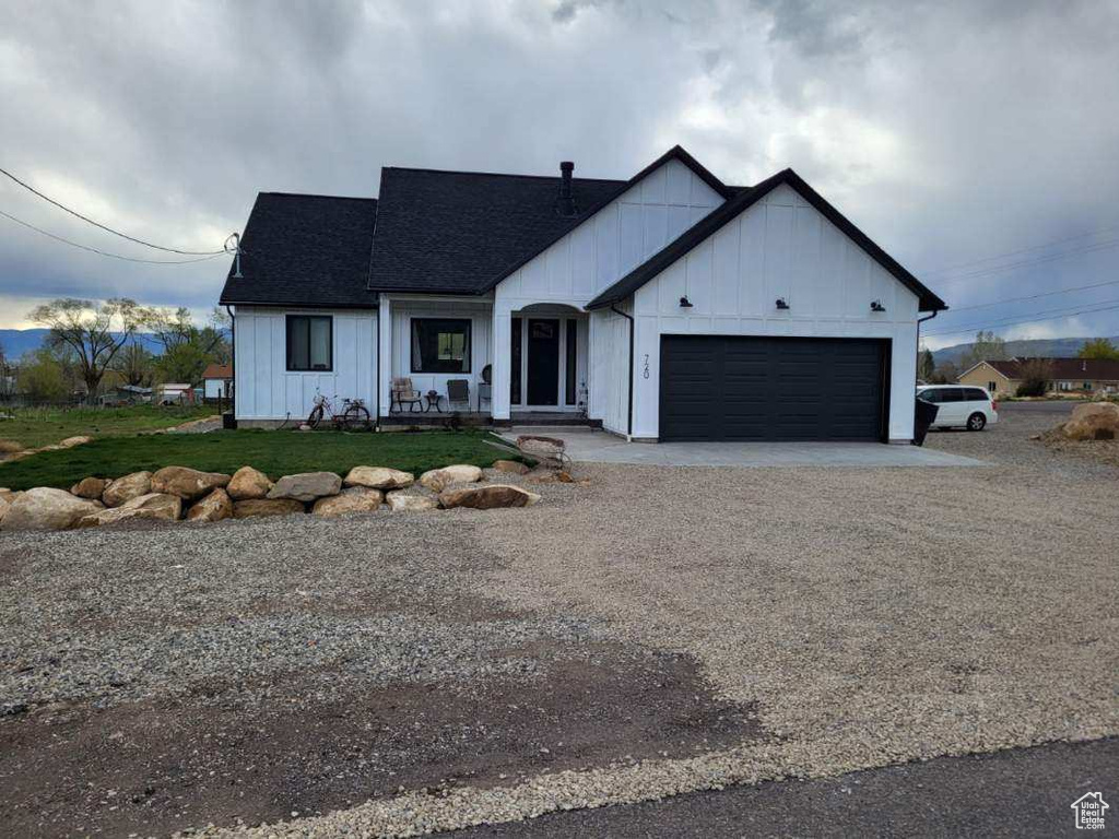 Modern farmhouse with board and batten siding, an attached garage, a front lawn, roof with shingles, and driveway