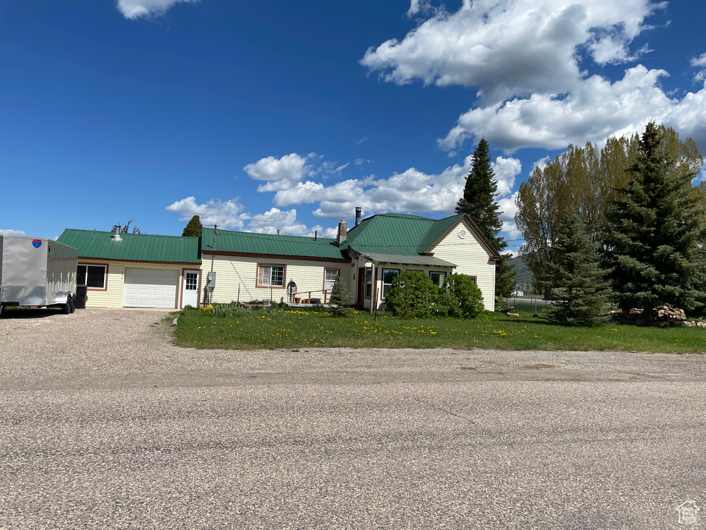 View of front of house with an attached garage, metal roof, dirt driveway, and a chimney