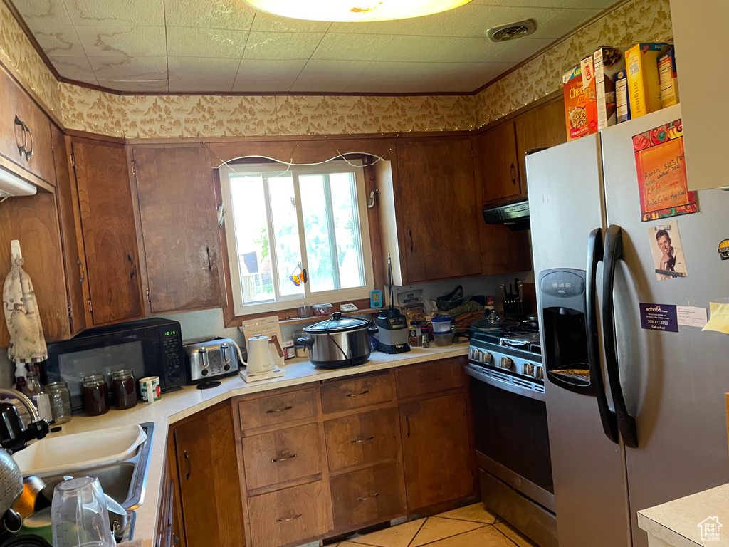 Kitchen with appliances with stainless steel finishes, under cabinet range hood, light countertops, and brown cabinets