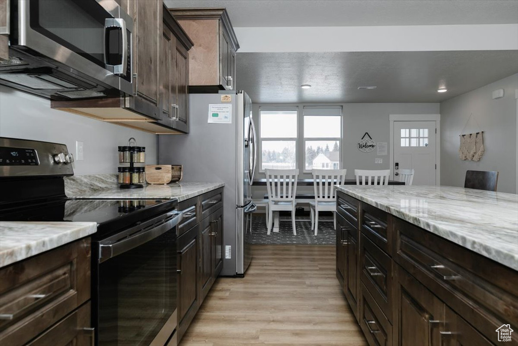 Kitchen with light stone counters, dark brown cabinets, stainless steel appliances, and light hardwood / wood-style floors