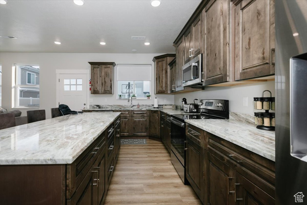 Kitchen featuring stainless steel appliances, dark brown cabinets, light stone counters, and light hardwood / wood-style floors