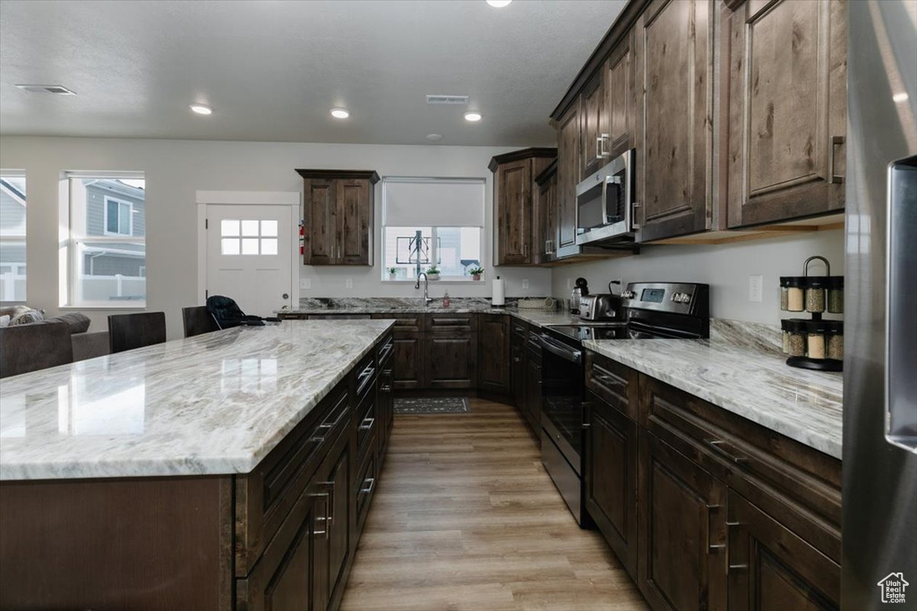 Kitchen with stainless steel appliances, light stone countertops, dark brown cabinetry, and light hardwood / wood-style flooring