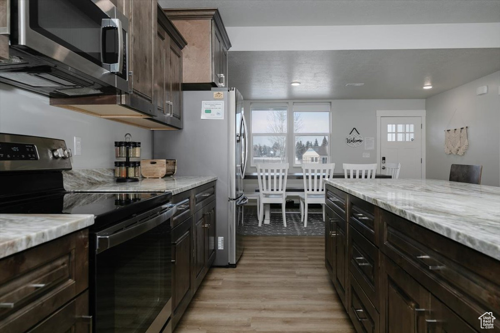 Kitchen with stainless steel appliances, light stone countertops, dark brown cabinets, and light wood-type flooring