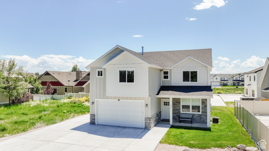 View of front of house with stone siding, an attached garage, a shingled roof, and concrete driveway