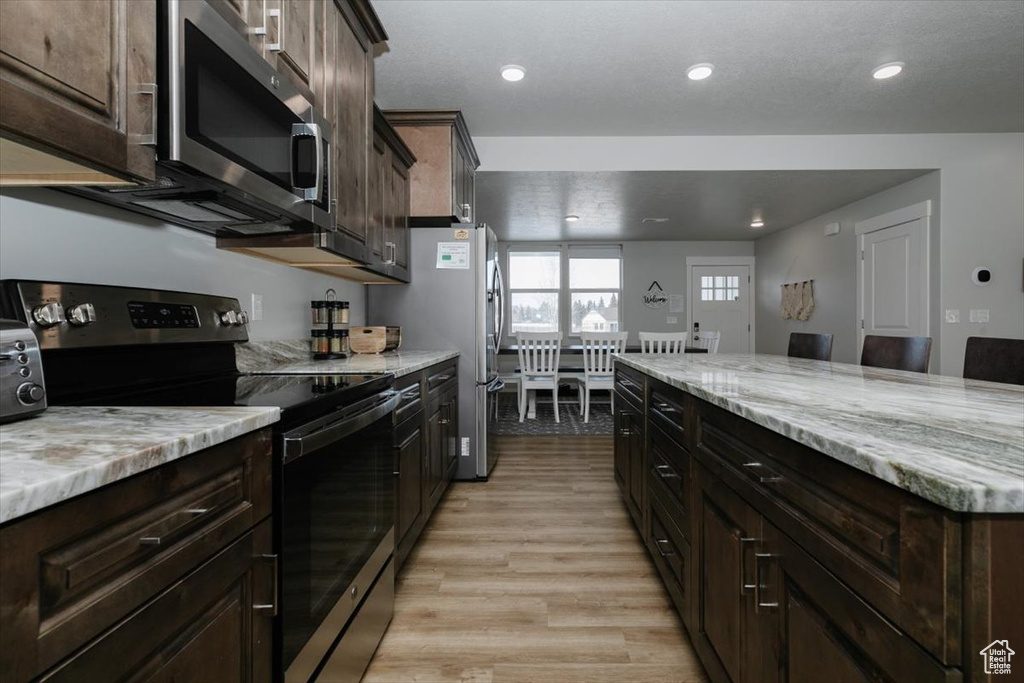 Kitchen featuring light stone counters, stainless steel appliances, dark brown cabinets, and light hardwood / wood-style flooring