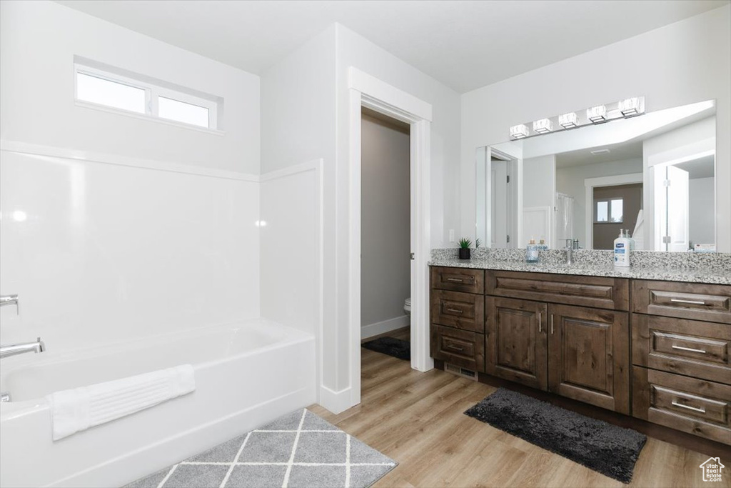 Bathroom with wood-type flooring, toilet, vanity, and a washtub