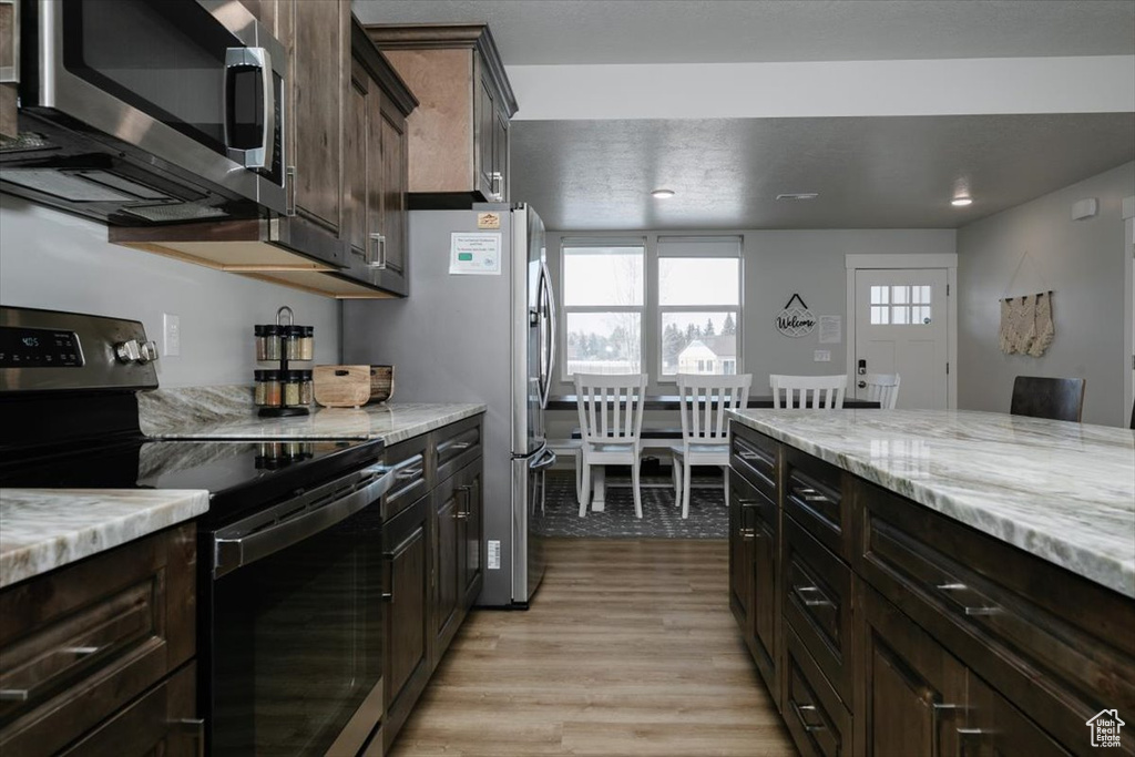 Kitchen with light stone countertops, dark brown cabinets, stainless steel appliances, and light hardwood / wood-style floors