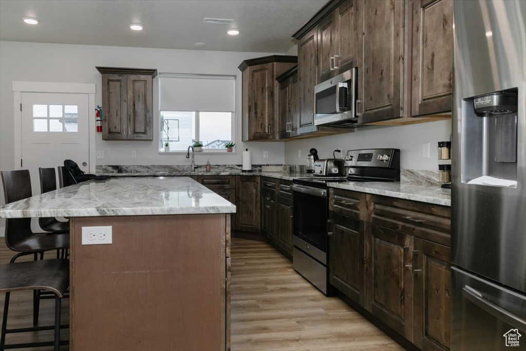 Kitchen with a kitchen island, a breakfast bar area, light hardwood / wood-style floors, stainless steel appliances, and light stone countertops