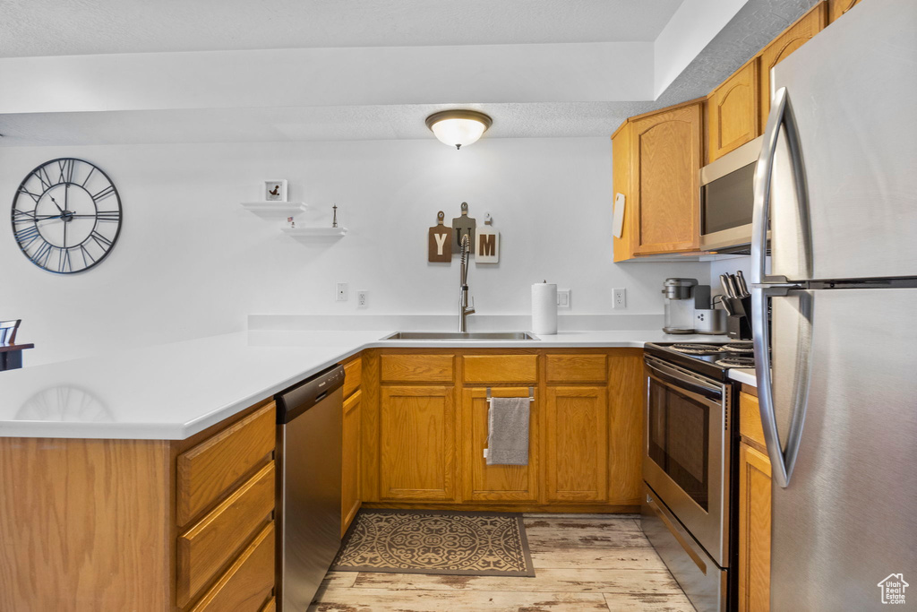 Kitchen featuring stainless steel appliances, sink, light hardwood / wood-style floors, and kitchen peninsula