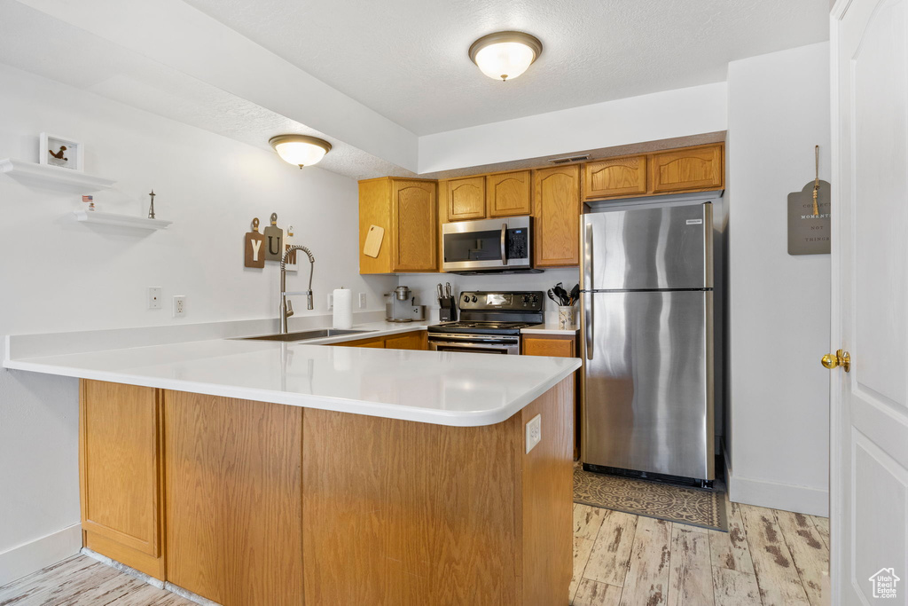 Kitchen with sink, light hardwood / wood-style floors, kitchen peninsula, stainless steel appliances, and a textured ceiling