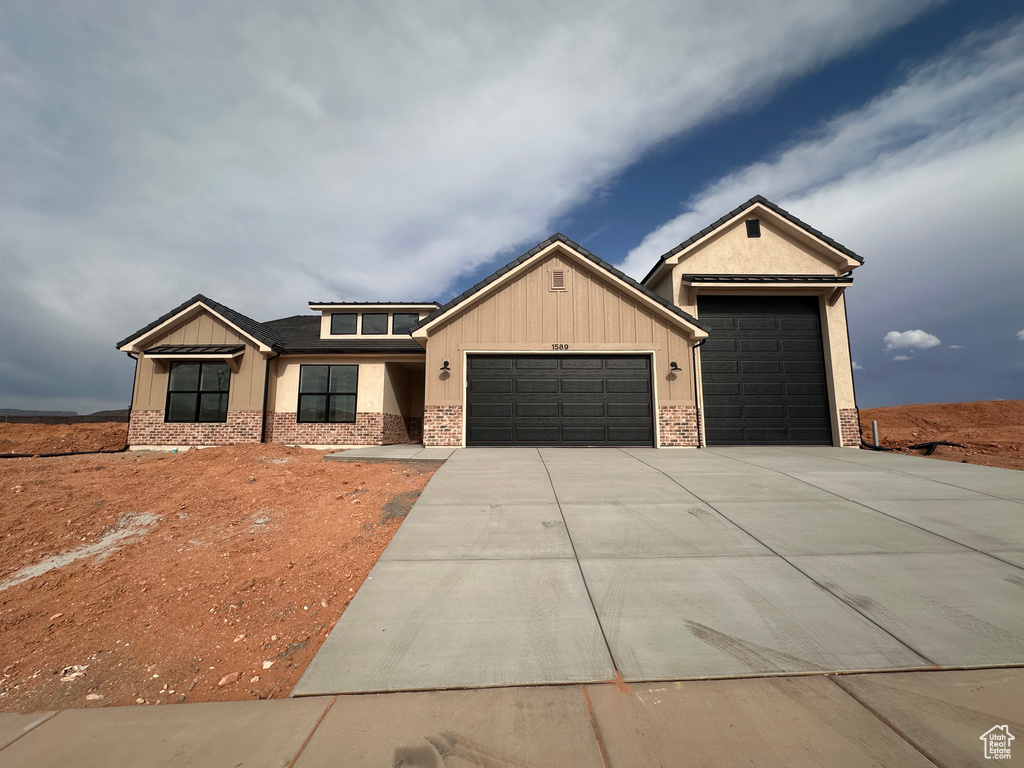 View of front of property featuring an attached garage, brick siding, driveway, and board and batten siding