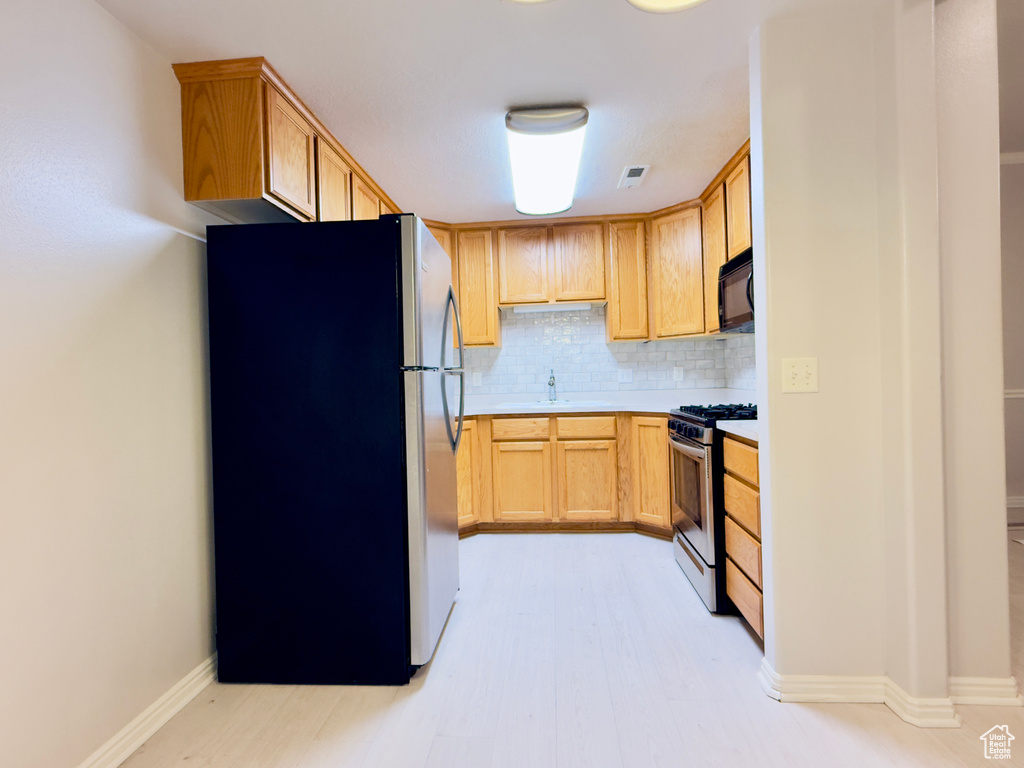Kitchen featuring appliances with stainless steel finishes, tasteful backsplash, light countertops, and light wood-type flooring