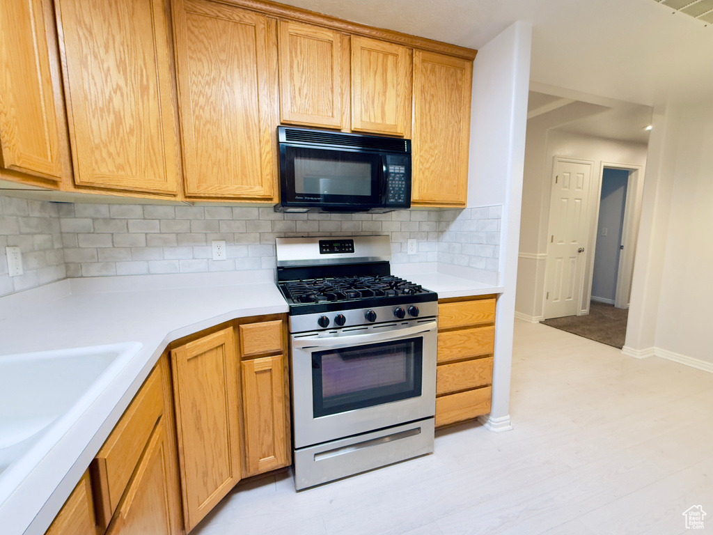 Kitchen with black microwave, gas stove, decorative backsplash, and light countertops
