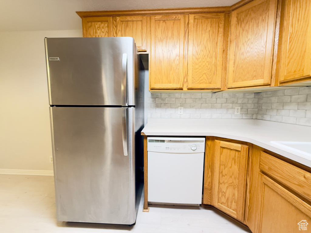 Kitchen with freestanding refrigerator, white dishwasher, tasteful backsplash, and light countertops