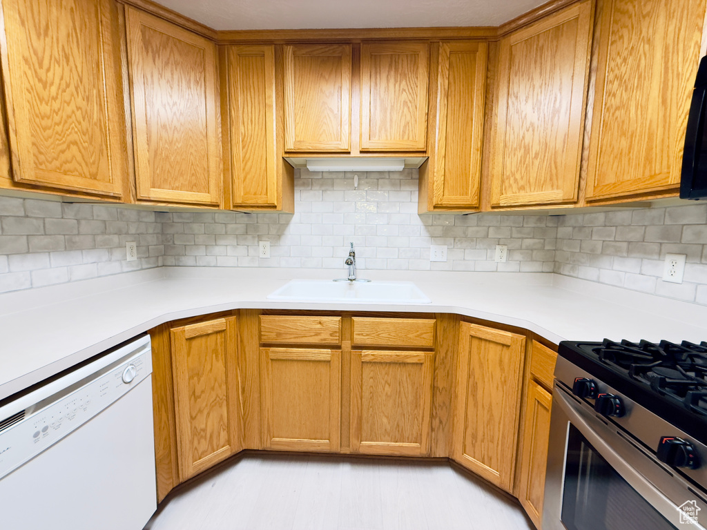Kitchen with white dishwasher, stainless steel range with gas stovetop, tasteful backsplash, and light countertops