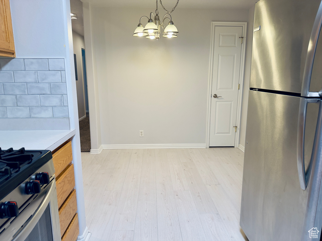 Kitchen with appliances with stainless steel finishes, light wood finished floors, a chandelier, light countertops, and tasteful backsplash