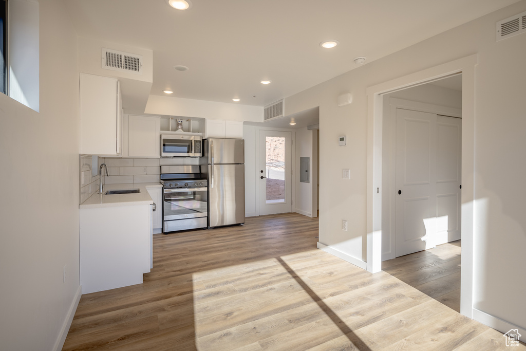 Kitchen featuring stainless steel appliances, a sink, light countertops, white cabinets, and light wood-style flooring