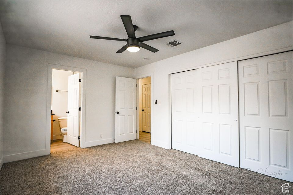 Unfurnished bedroom featuring ceiling fan, light carpet, ensuite bath, and a closet