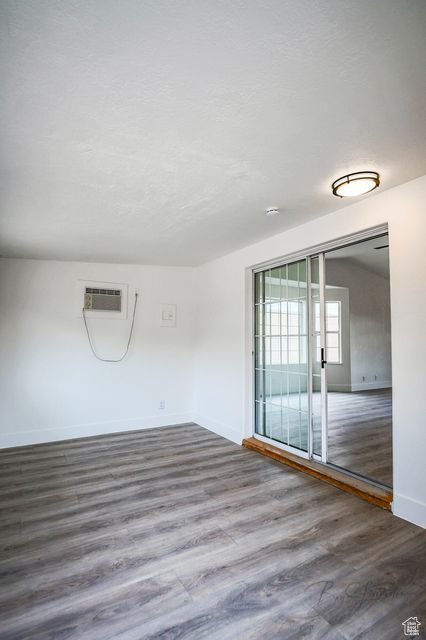Unfurnished room featuring hardwood / wood-style floors and an AC wall unit