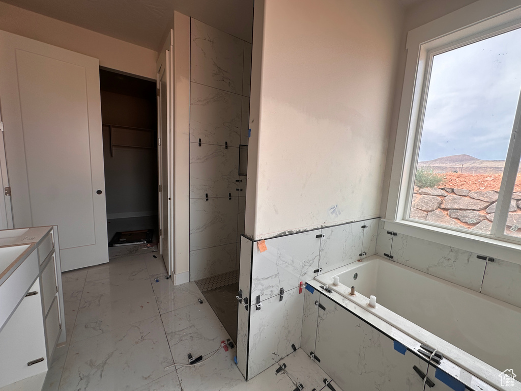 Bathroom featuring marble finish flooring, a bath, vanity, and a spacious closet