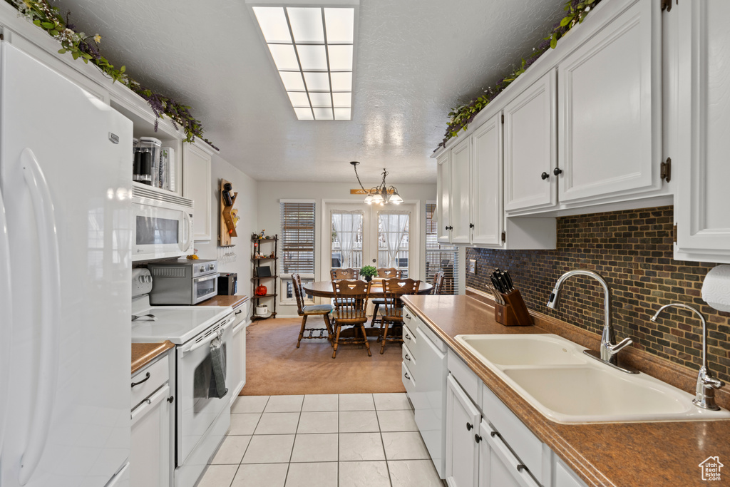 Kitchen featuring white appliances, white cabinetry, light carpet, and a sink