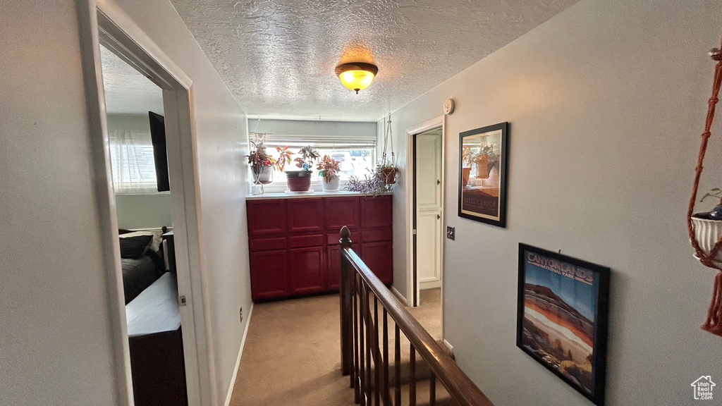 Corridor featuring a textured ceiling, an upstairs landing, and light carpet