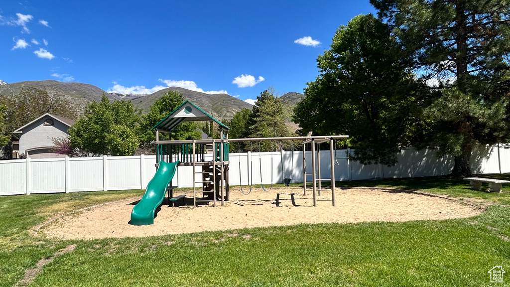View of jungle gym with a lawn, fence, and a mountain view