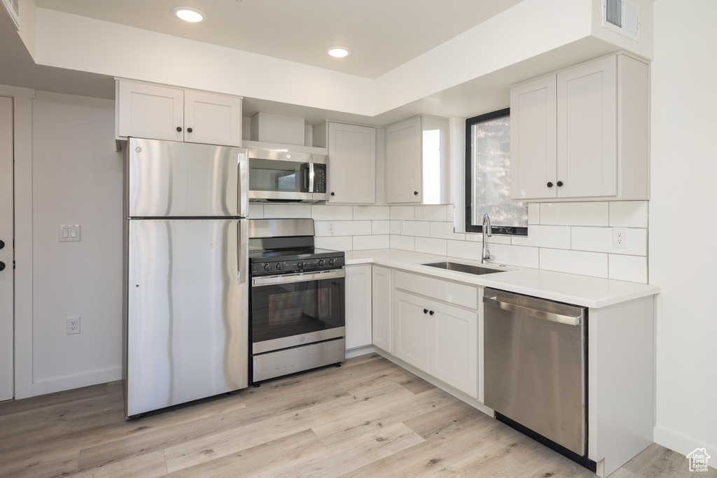Kitchen featuring stainless steel appliances, a sink, decorative backsplash, light wood-style flooring, and recessed lighting