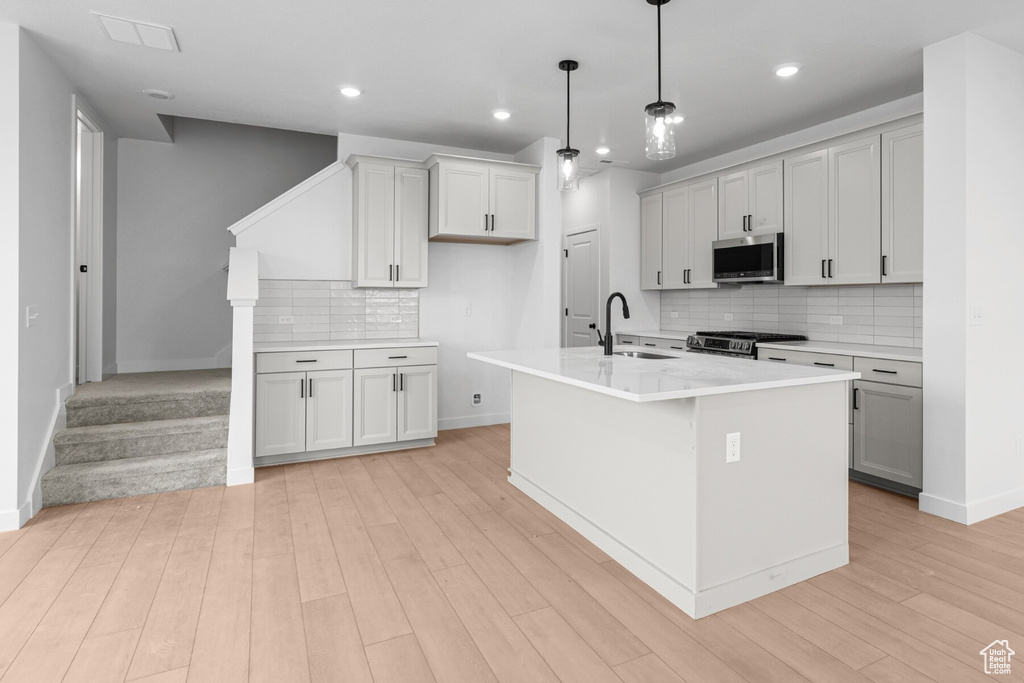 Kitchen featuring sink, hanging light fixtures, stainless steel appliances, a center island with sink, and light wood-type flooring