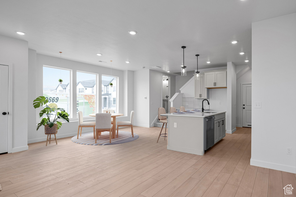 Kitchen featuring pendant lighting, dishwasher, an island with sink, sink, and white cabinets