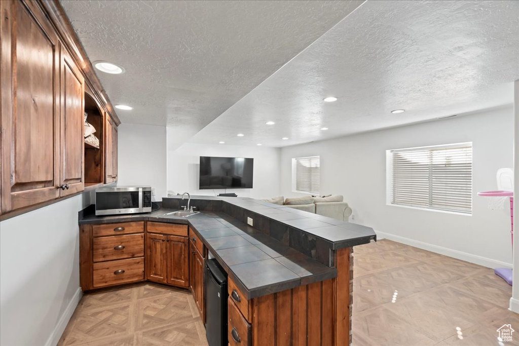 Kitchen featuring sink, tile countertops, a textured ceiling, kitchen peninsula, and light parquet flooring